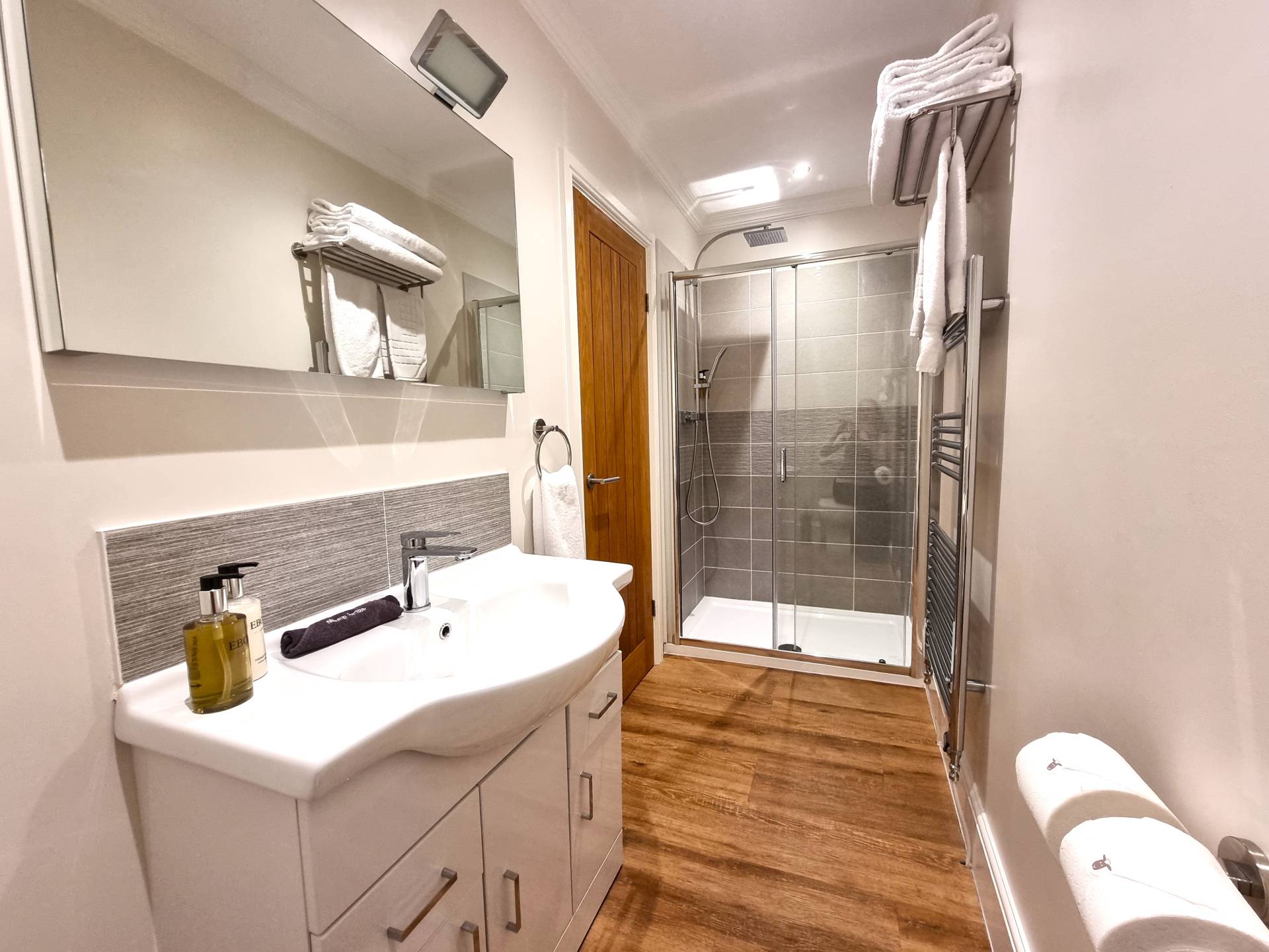 En-suite bathroom in first-floor sea view Room 101 at Min y Don Llandudno with walk-in shower, plush towels, heated towel radiator, vanity unit with makeup remover cloth, Ebony hand and body wash and moisturiser, and heated mirror with shaver and toothbrush charger.